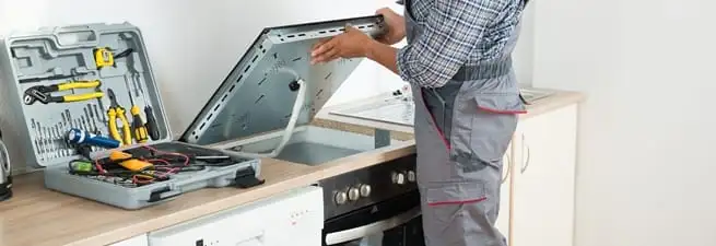 Cooktop repair technician lifting a built-in stovetop for service in Oakland, CA