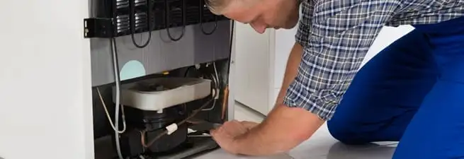 Refrigerator repair technician servicing the compressor and condenser area in Oakland, CA