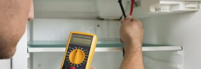 Refrigerator repair technician testing electrical components with a multimeter in Oakland, CA