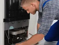 Refrigerator repair technician servicing the compressor and condenser area in Oakland, CA