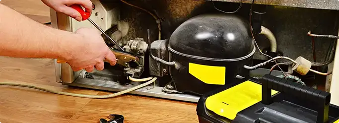 Refrigerator repair technician fixing the compressor and wiring in Oakland, CA